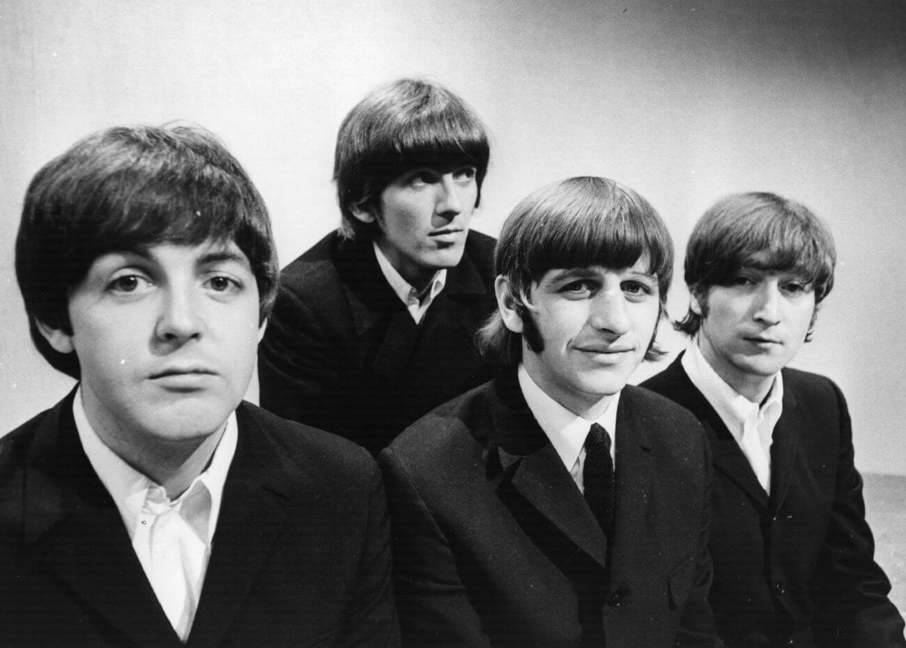 A black and white picture of the musicians Paul McCartney, George Harrison, Ringo Starr, and John Lennon of The Beatles sitting in a line.