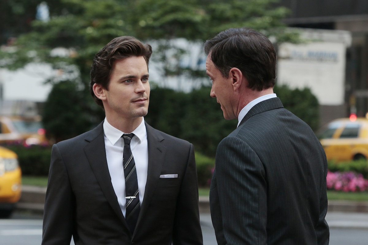 Matt Bomer, in a black suit, talking to a man in 'White Collar'
