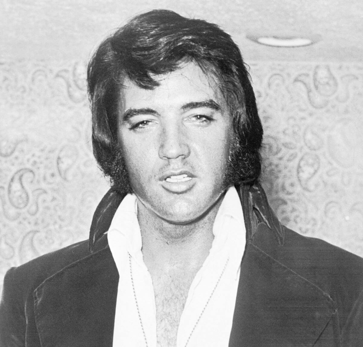 A black and white picture of Elvis Presley wearing a white shirt and black jacket.