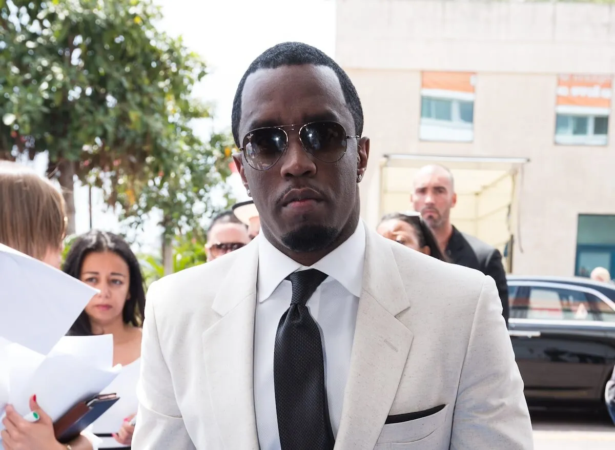 Sean 'Diddy' Combs in a white suit standing outside looking at the camera