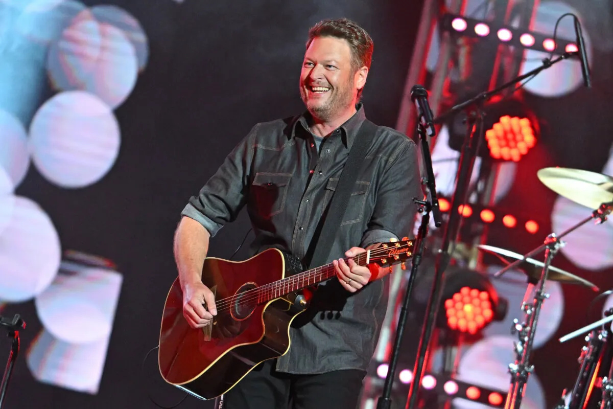 Blake Shelton wears a gray shirt and plays guitar.