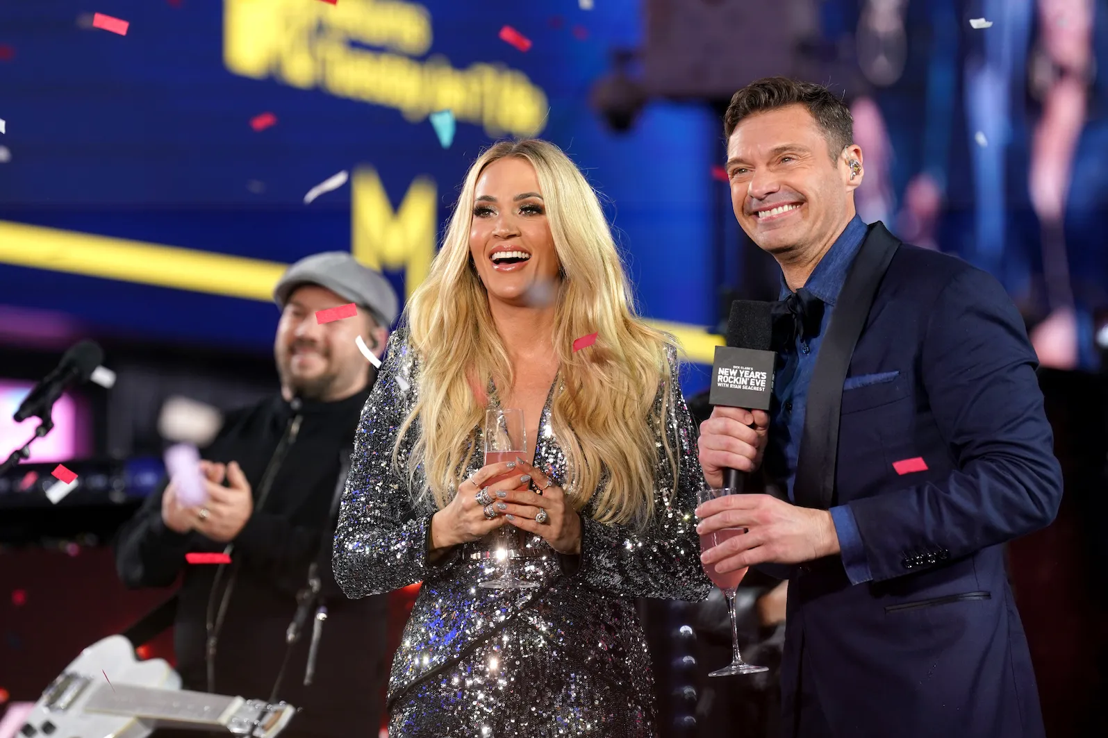 'American Idol' judge Carrie Underwood and host Ryan Seacrest smiling and holding microphones as confetti falls around them during New Year's Eve special