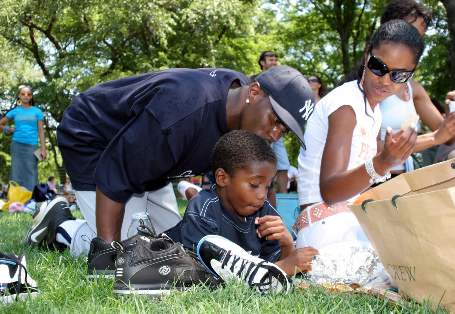 Sean 'Diddy' Combs, Kim Porter, and Christian 'King' Combs sitting together in the grass in 2005. Diddy is kissing Christian's head. Porter is sitting next to them and watching.