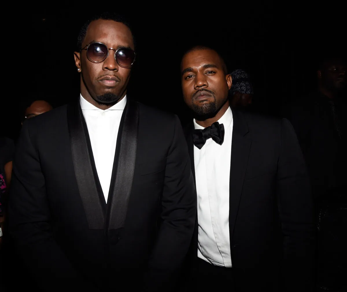Sean 'Diddy' Combs wears a suit and sunglasses and stands with Kanye West, who wears a tuxedo.